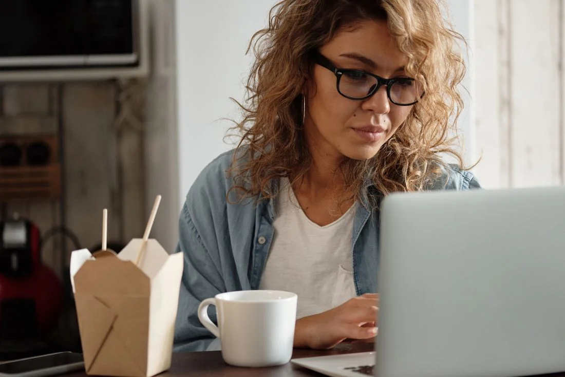 Woman in an open denim shirt and white T-shirt at a laptop.