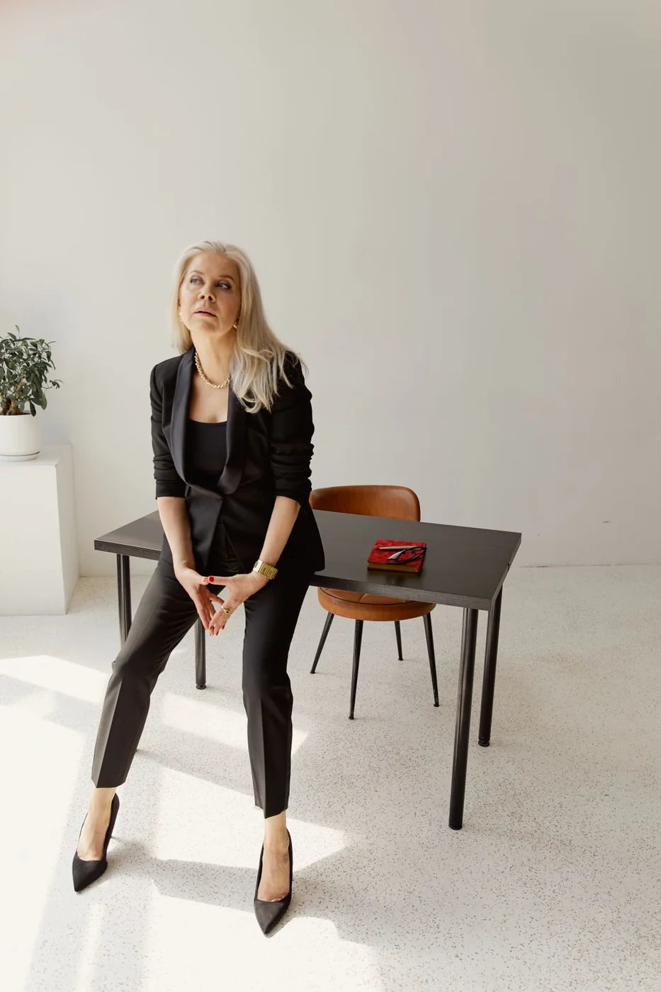 Woman in a black blazer and trousers seated in an office.