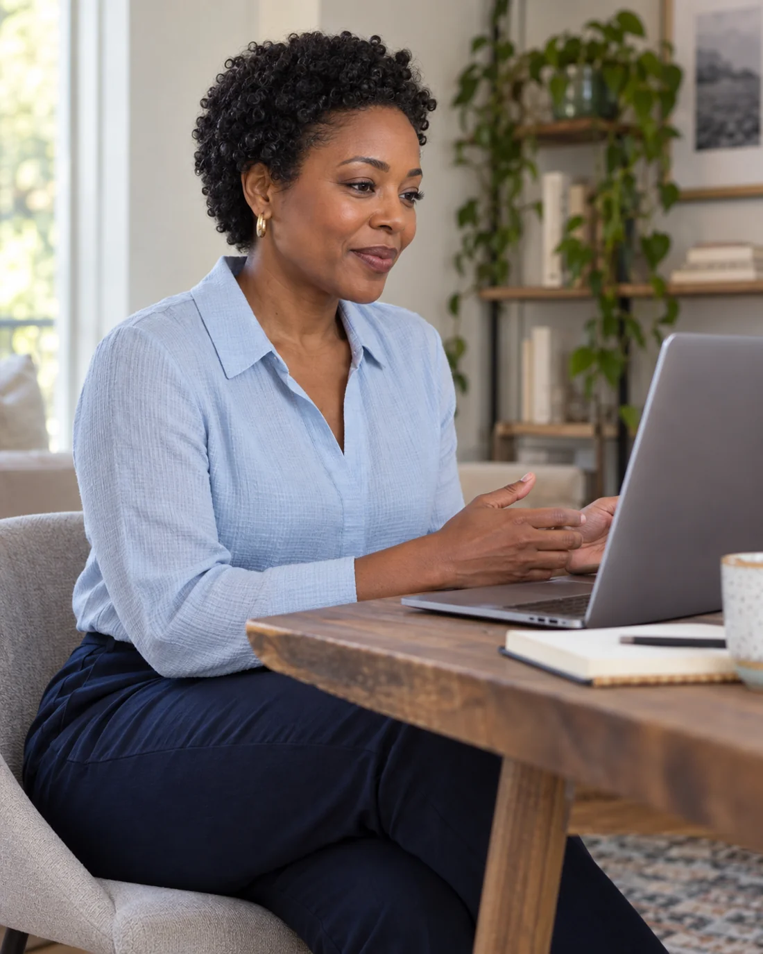 Woman in a pale blue blouse seated at a laptop for a video call.