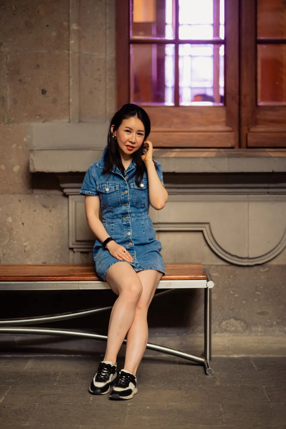 Woman in a denim dress and closed shoes on a museum bench.