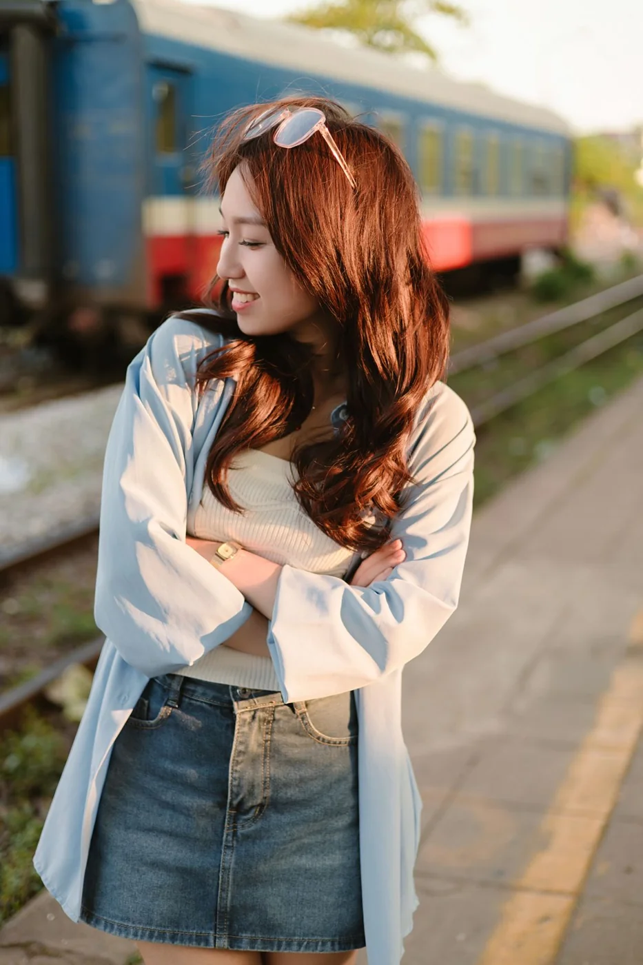 Woman in a denim skirt and light cardigan on a train platform.