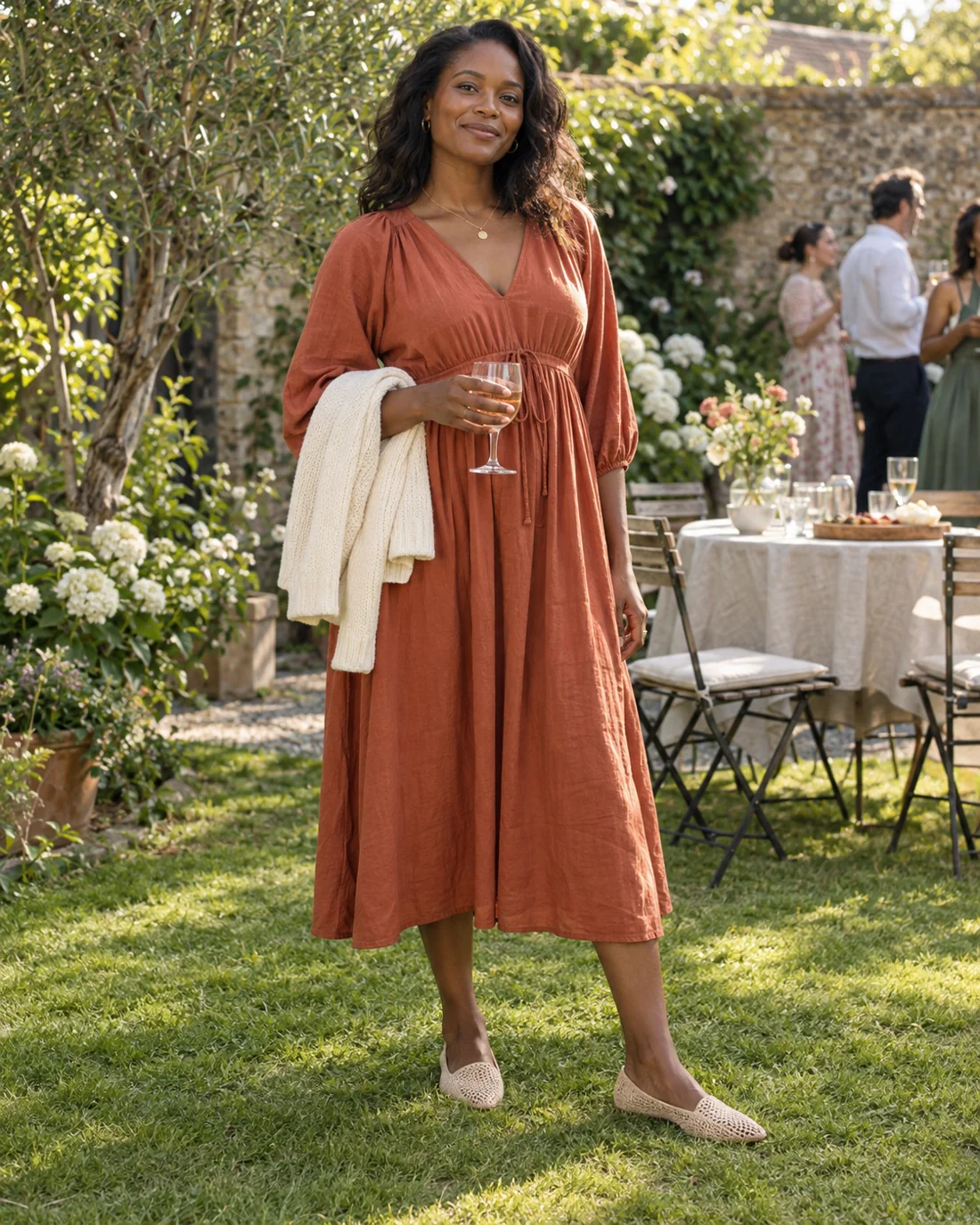 Woman in a terracotta dress and flat shoes on a garden lawn.