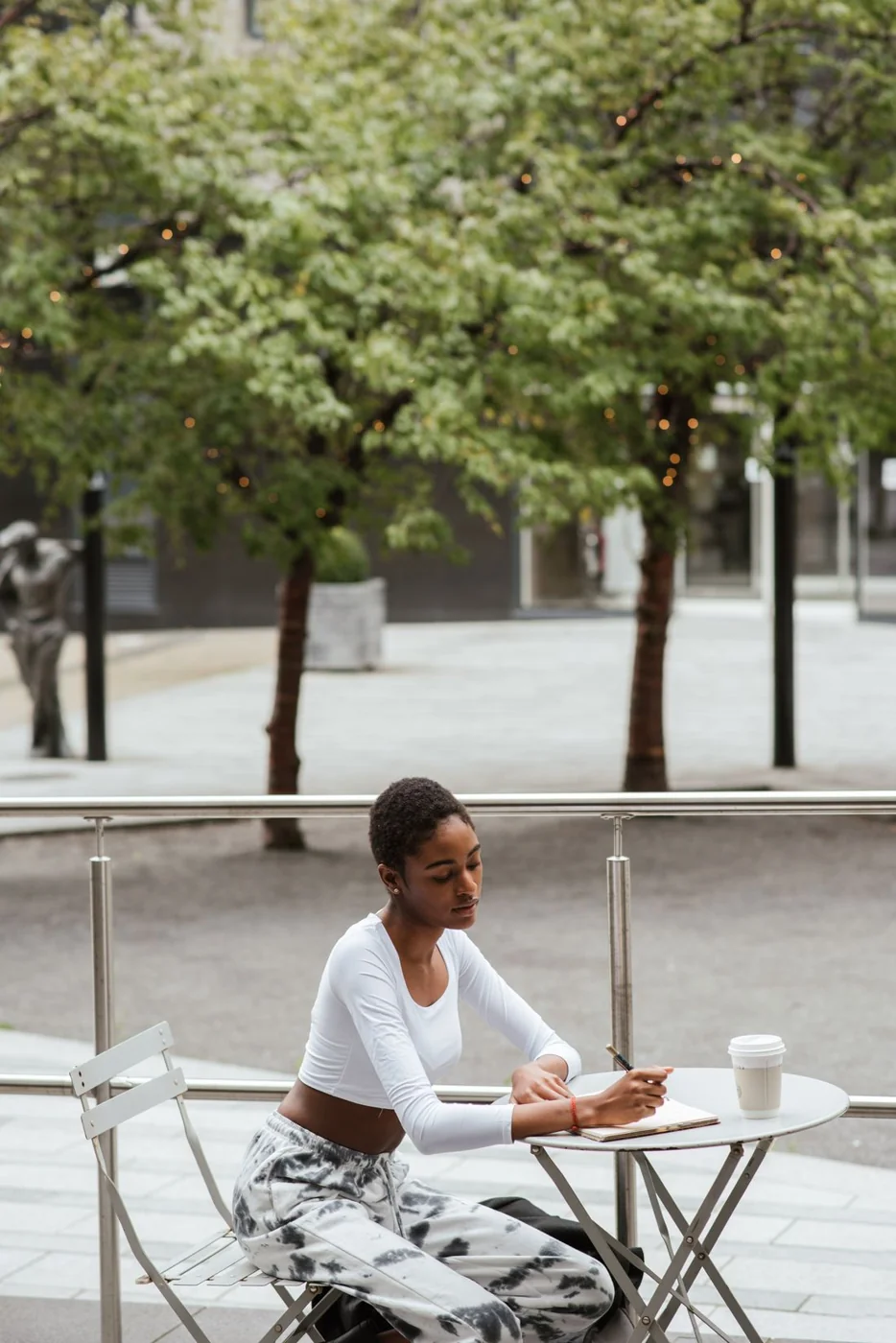 Woman in a white top and patterned trousers at an outdoor café.