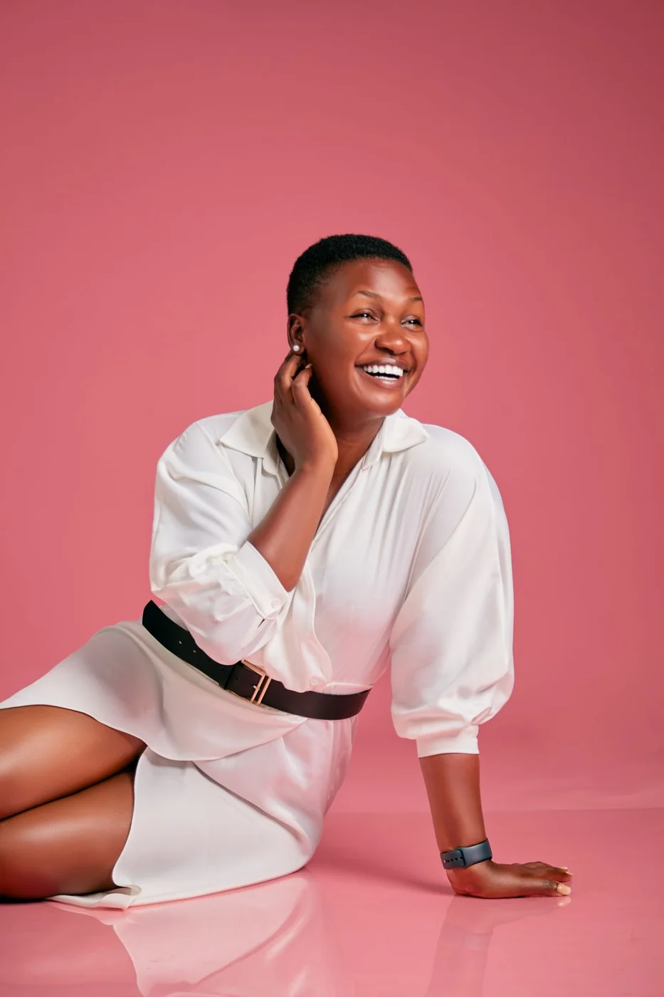 Woman wearing a white shirt dress with a black belt.