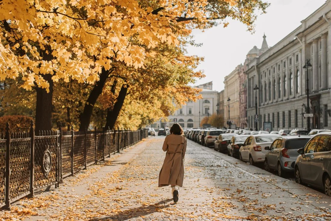 Woman in a long trench coat on an autumn pavement.