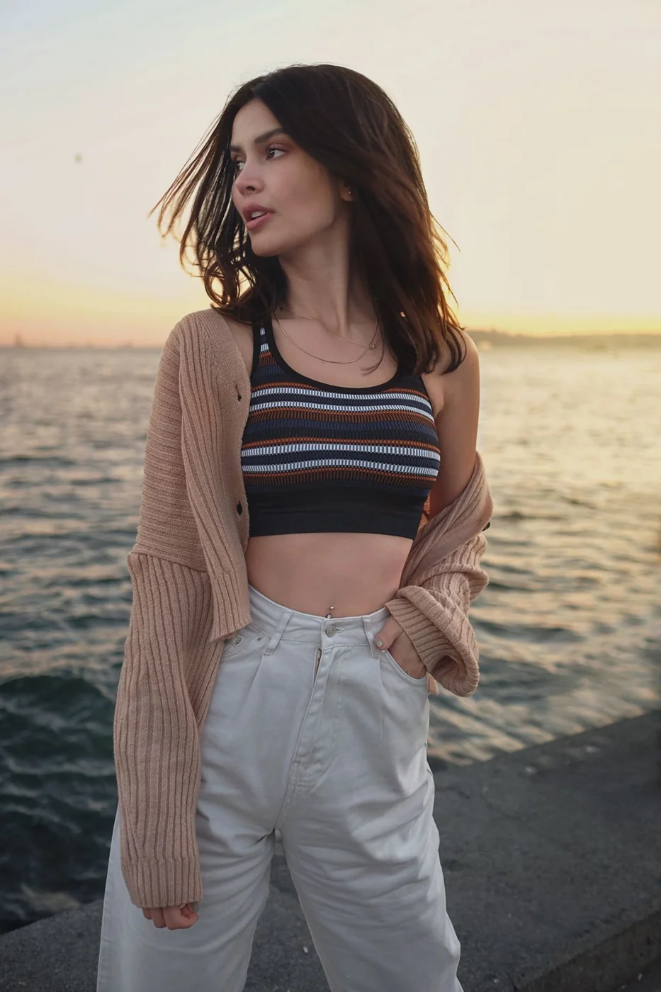 Woman in a cardigan and striped top by the sea.
