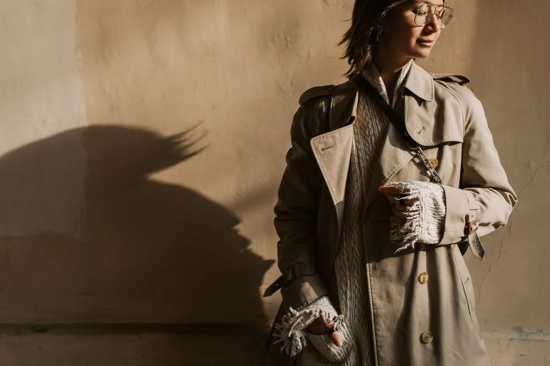 Beige trench coat over a light knitted jumper.