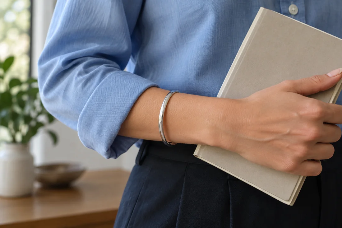 A silver-coloured bangle below the turned-back sleeve of a blue shirt.