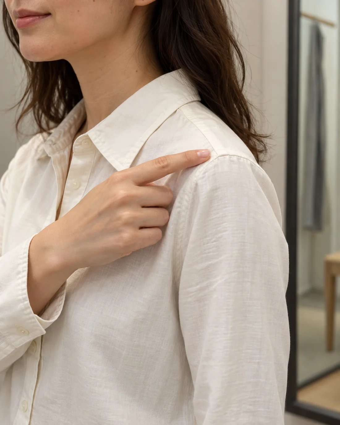 Close view of a shoulder seam on a pale shirt, with a hand pointing to the seam.