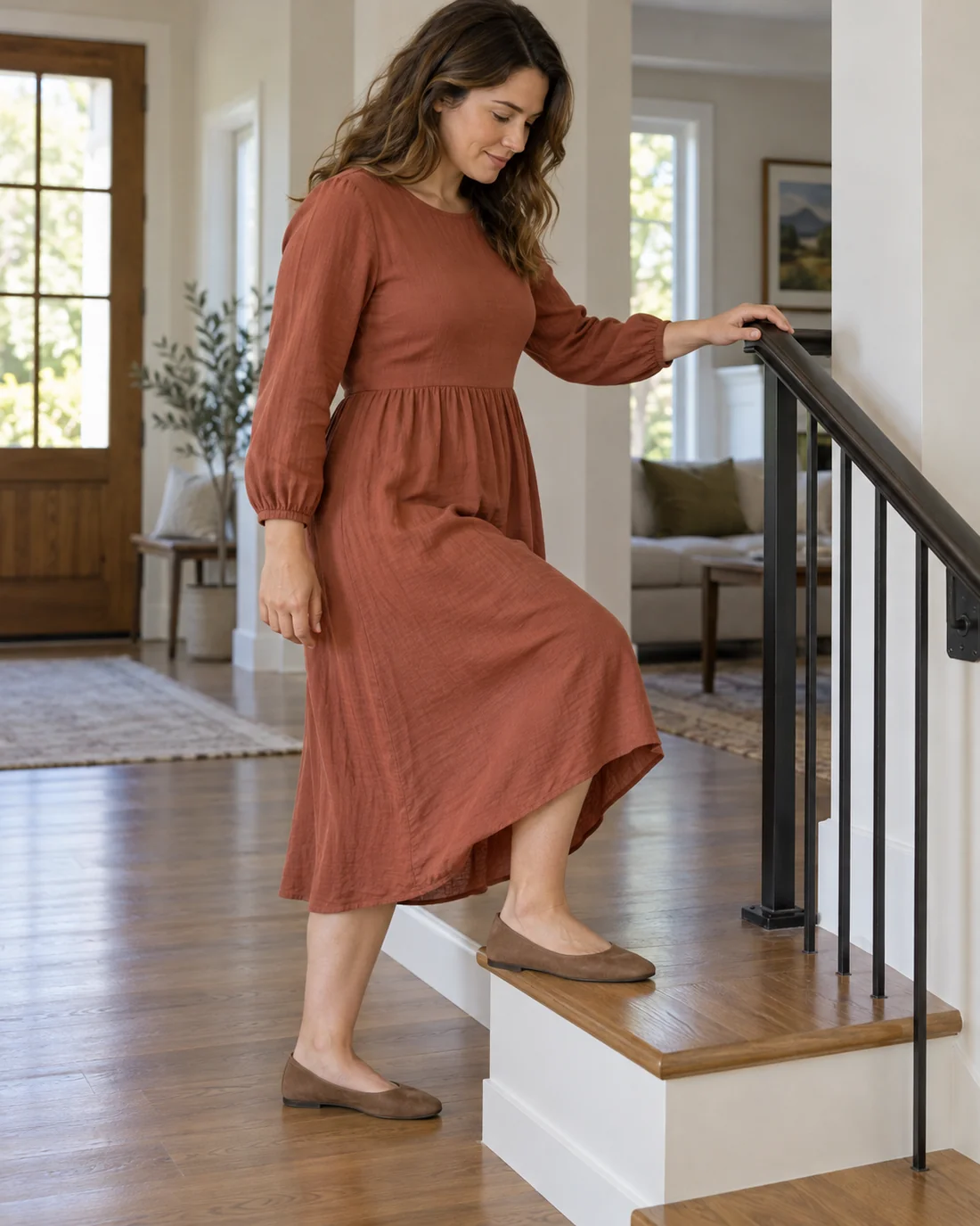 Woman in a rust midi dress stepping onto a low stair with one hand on the rail.