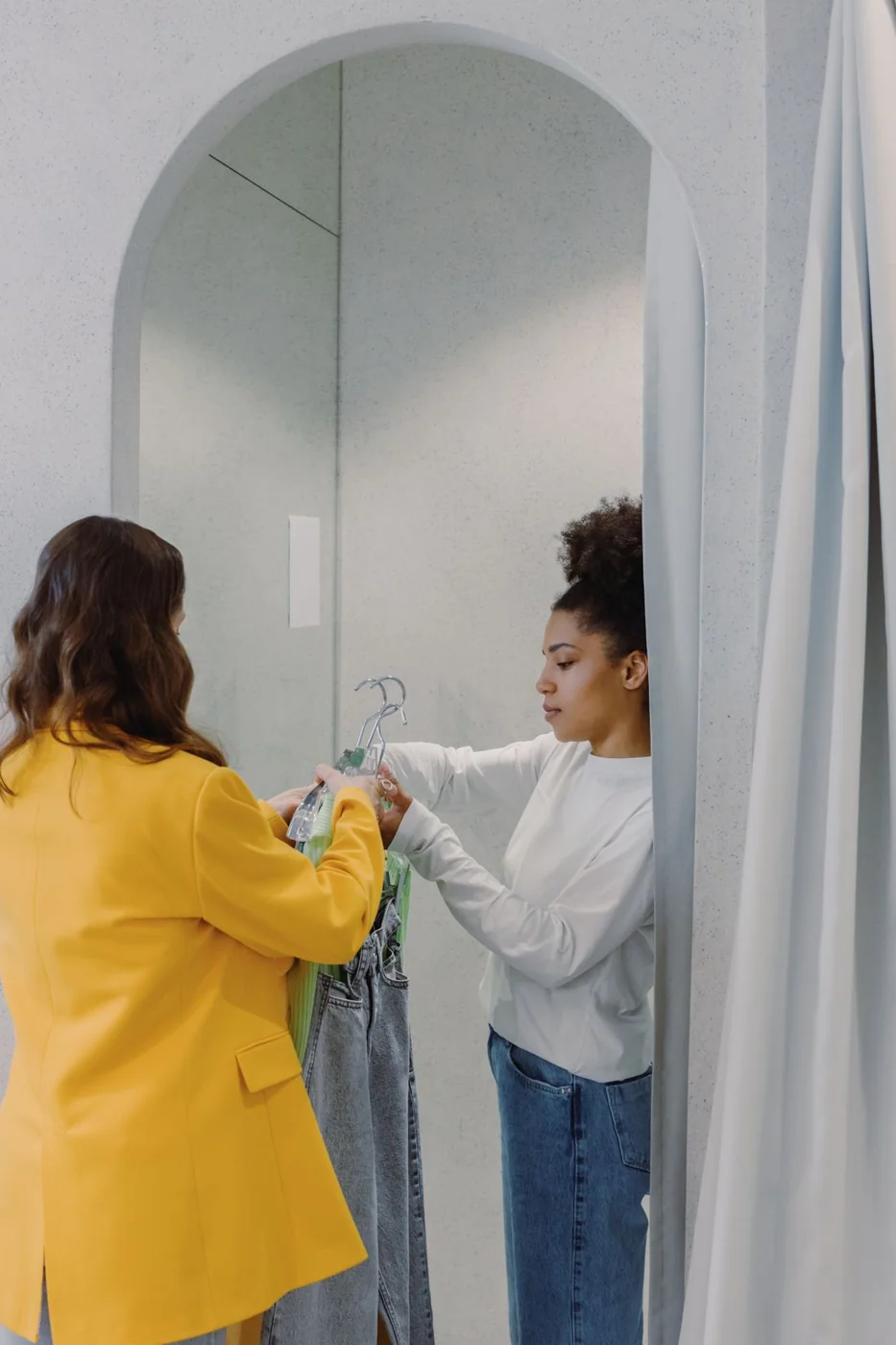 Two women comparing garments in a fitting room.